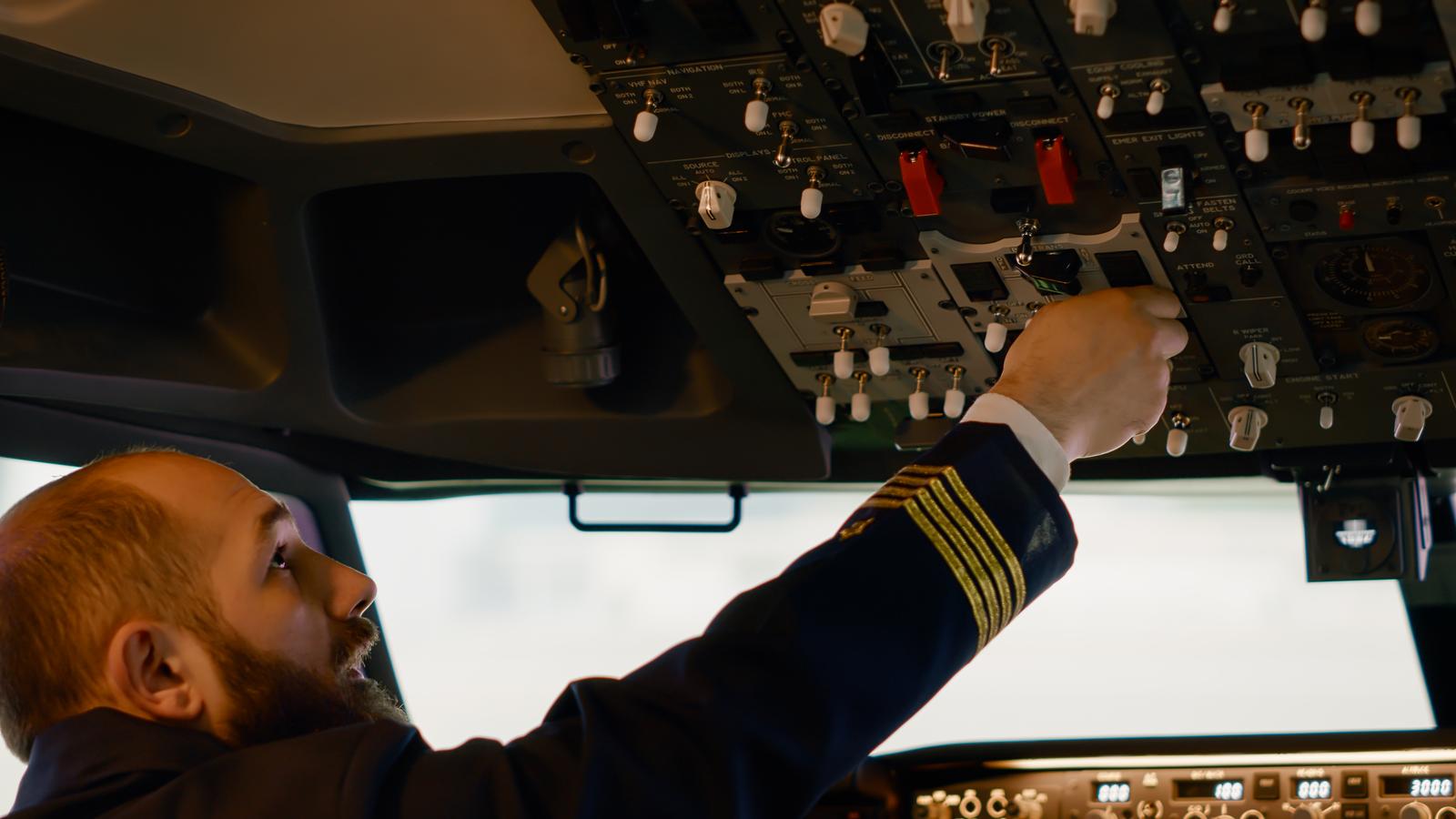Airplane captain starting engine with power buttons on dashboard